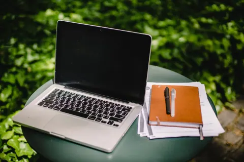 Laptop and notebook on a round table with a green garden in the background