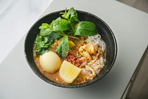 Bowl of noodles with fresh herbs, lime, and a savory broth